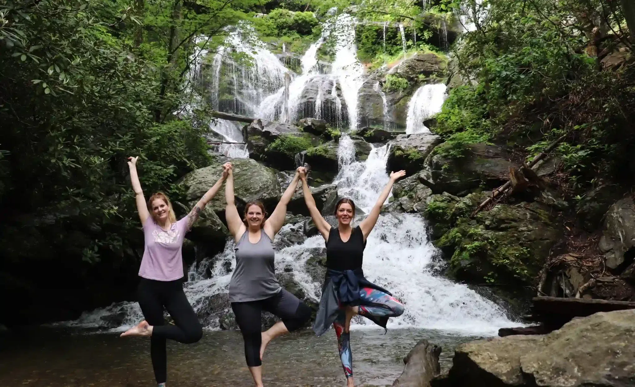 A Yoga Angels group practising tree pose in front of a waterfall