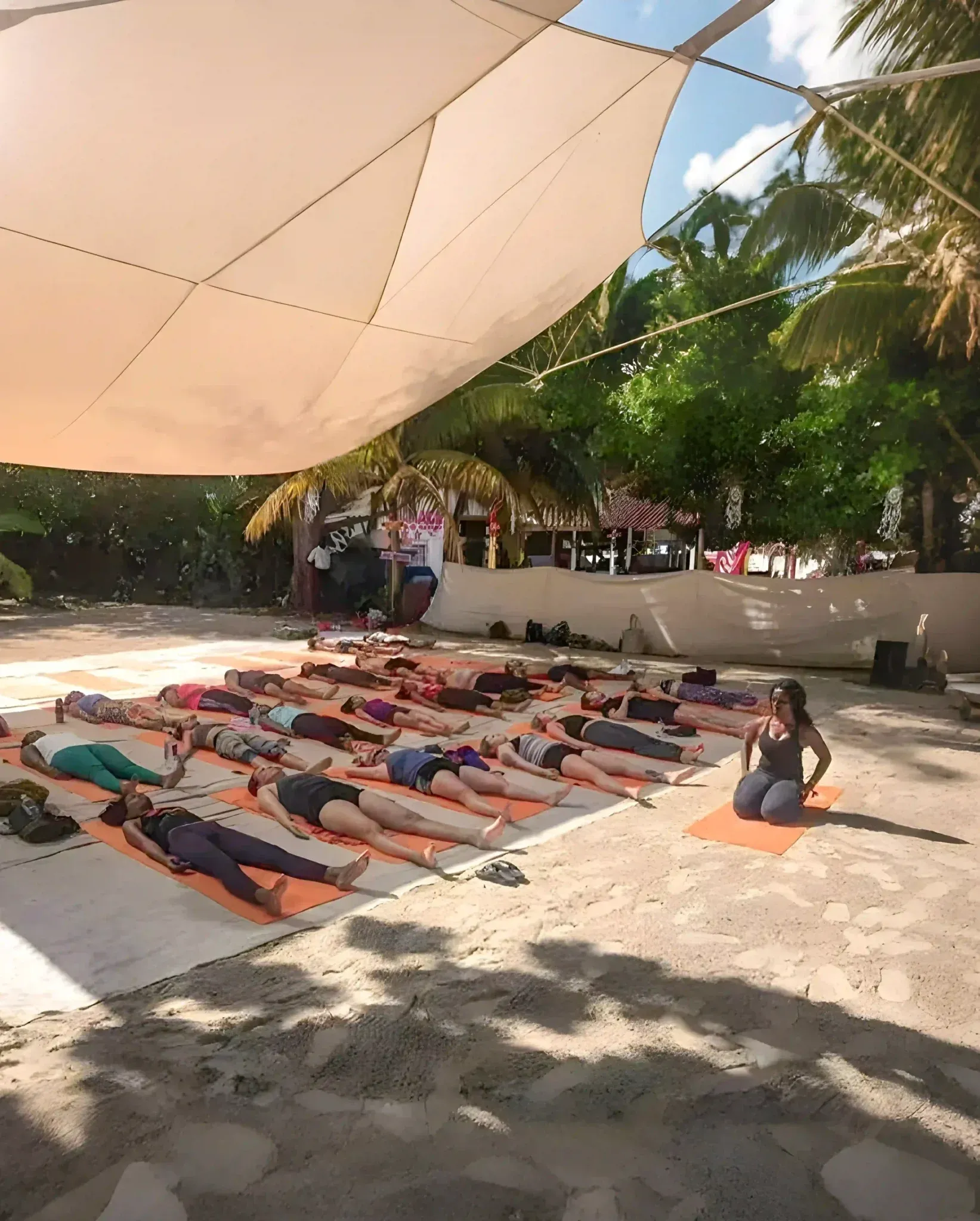 A class lying on mats in deep relaxation under a shade sail at the Oasis while the teacher guides them